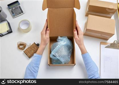 delivery, mail service, people and shipment concept - female hands packing mug into parcel box with protective bubble wrap at post office. hands packing mug to parcel box at post office