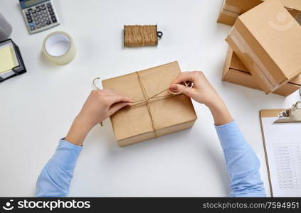 delivery, mail service, people and shipment concept - female hands packing parcel box and tying rope at post office. female hands packing parcel box at post office