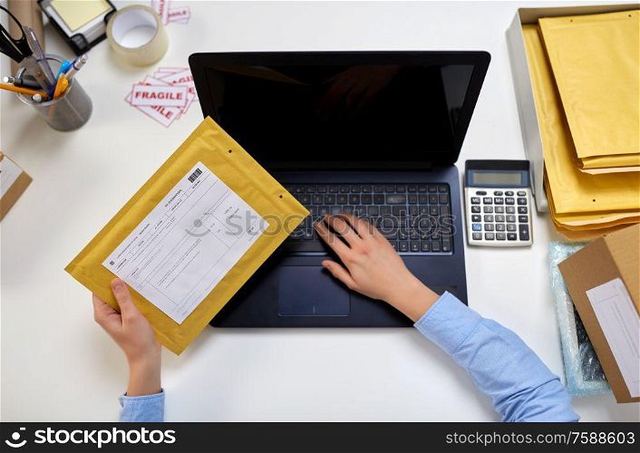 delivery, mail service, people and shipment concept - female hands with laptop computer and envelope parcel with postal form on it at post office. hands with laptop and envelope at post office