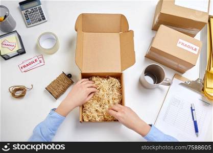 delivery, mail service, people and shipment concept - female hands with straw filler in parcel box at post office. hands with straw filler in parcel at post office