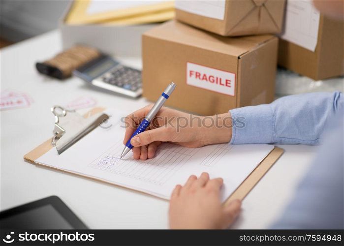 delivery, mail service, people and shipment concept - hands with clipboard filling checklist at post office. hands with clipboard and parcels at post office