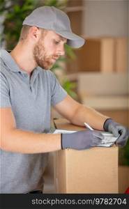 delivery man fills in paperwork leaning on cardboard box