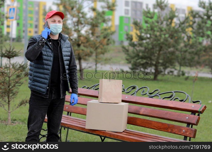 Delivery man in red hat, protection mask and medical rubber gloves with parcels using smartphone to sending to customer. Delivery man in red hat, protection mask and medical rubber gloves with parcels using smartphone to sending to customer. delivery service