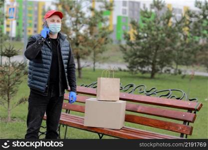 Delivery man in red hat, protection mask and medical rubber gloves with parcels using smartphone to sending to customer. Delivery man in red hat, protection mask and medical rubber gloves with parcels using smartphone to sending to customer. delivery service