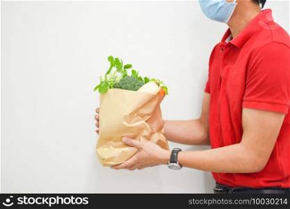 Delivery man wearing protective face mask coronavirus and hand holding craft paper food packaging bag service with fresh vegetable, Postman express for takeaway food delivery service to home