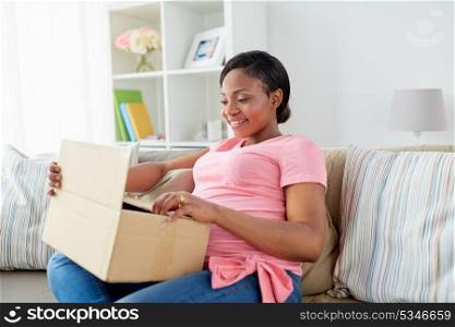 delivery, people and pregnancy concept - happy pregnant african american woman opening parcel box at home. happy pregnant woman opening parcel box at home