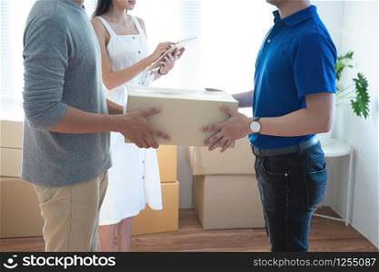 Delivery service worker in uniform delivering parcels to happy asian couple. Woman with tablet signing proof document.shopping online and home delivery concept.