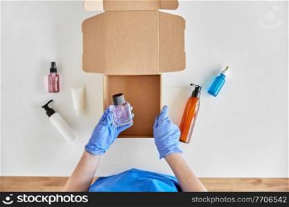 delivery, shipping and pandemic concept - hands in protective medical gloves packing parcel box with cosmetics and beauty products. hands in gloves packing parcel box with cosmetics