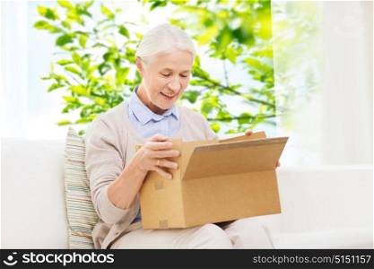 delivery, shipping and people concept - happy smiling senior woman looking into open parcel box at home over window and green natural background. happy senior woman with parcel box at home