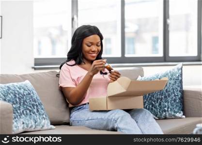 delivery, shipping and people concept - happy young african american woman opening parcel box with cosmetcis at home. african american woman opening parcel box at home