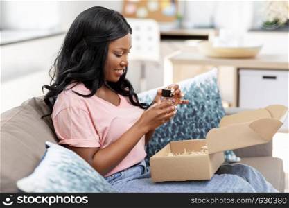 delivery, shipping and people concept - happy young african american woman opening parcel box with perfume at home. african american woman opening parcel box at home
