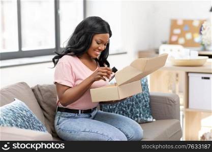 delivery, shipping and people concept - happy young african american woman opening parcel box with perfume at home. african american woman opening parcel box at home