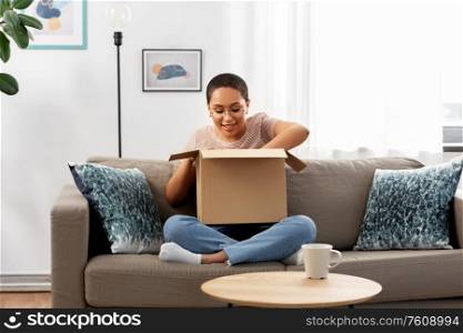 delivery, shipping and people concept - happy young african american woman opening parcel box at home. african american woman opening parcel box at home