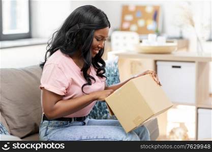 delivery, shipping and people concept - happy young african american woman opening parcel box at home. african american woman opening parcel box at home