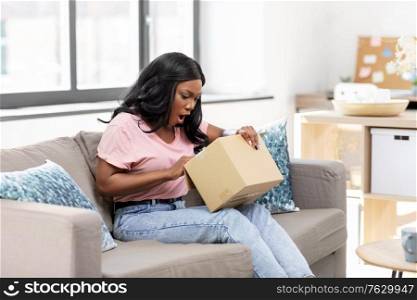 delivery, shipping and people concept - surprised young african american woman opening parcel box at home. african american woman opening parcel box at home