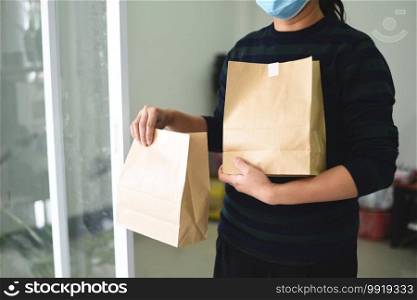 Delivery woman wearing protective face mask coronavirus and hand holding craft paper food packaging bag service, Postman express for takeaway food delivery service to home