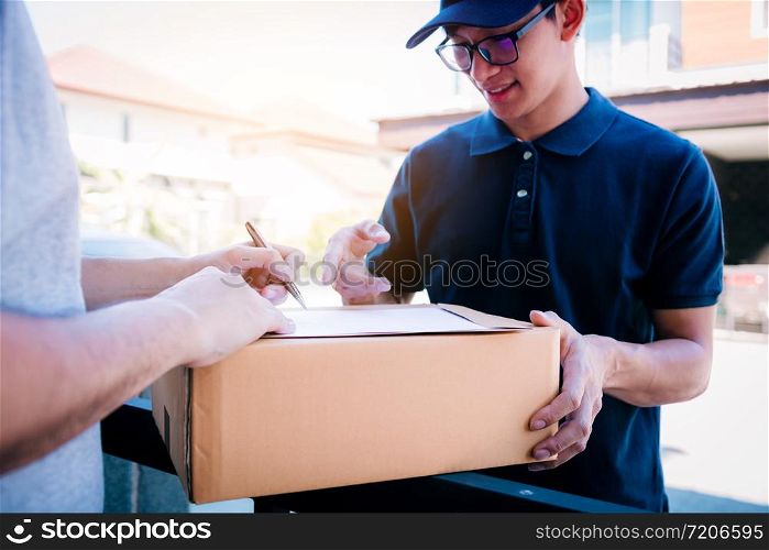 Delivery young man standing at the door of home and carrying parcels for young male to signing.