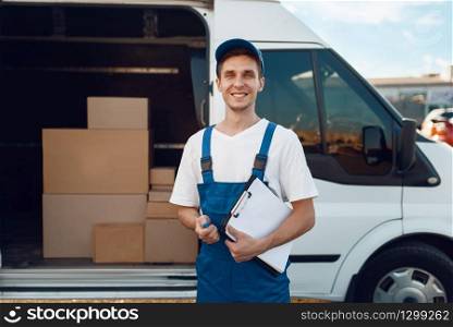 Deliveryman in uniform, carton boxes in the car, delivery service. Man standing at cardboard packages in vehicle, male deliver, courier or shipping job. Deliveryman in uniform, carton boxes in the car