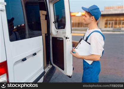 Deliveryman in uniform closing the car, delivery service, delivering. Man in post vehicle, male deliver, courier or shipping job