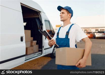 Deliveryman in uniform gives parcel, carton boxes in the car, delivery service. Man standing at cardboard packages in vehicle, male deliver, courier or shipping job. Deliveryman in uniform gives parcel, delivery