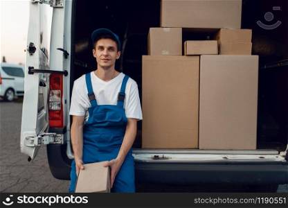 Deliveryman in uniform gives parcel to female buyer at the car, delivery service, delivering. Man holding cardboard package near the vehicle, male deliver and woman, courier or shipping job. Deliveryman gives parcel to buyer, delivering