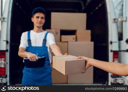 Deliveryman in uniform gives parcel to female buyer at the car, delivery service, delivering. Man holding cardboard package near the vehicle, male deliver and woman, courier or shipping job