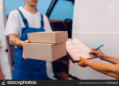 Deliveryman in uniform gives parcel to female recipient at the car, delivery service. Man holding cardboard package near the vehicle, male deliver and woman, courier or shipping job. Deliveryman gives parcel to female recipient