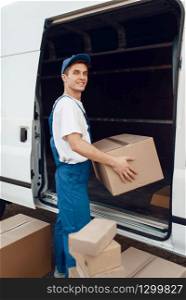 Deliveryman in uniform unloads the car with parcels, delivery service. Man standing at cardboard packages in vehicle, male deliver, courier or shipping job. Deliveryman unloads the car with parcels, delivery