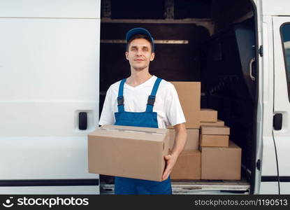 Deliveryman with carton box at the car, delivery service. Man in uniform holding cardboard package, male deliver, courier job