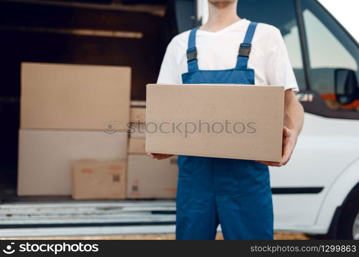 Deliveryman with carton box at the car, delivery service. Man in uniform holding cardboard package, male deliver, courier job. Deliveryman with carton box at the car, delivery