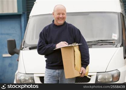 Deliveryperson standing with van with clipboard and box smiling