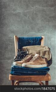 Denim jeans and old boots at chair. Stack of jeans near abstract background texture surface