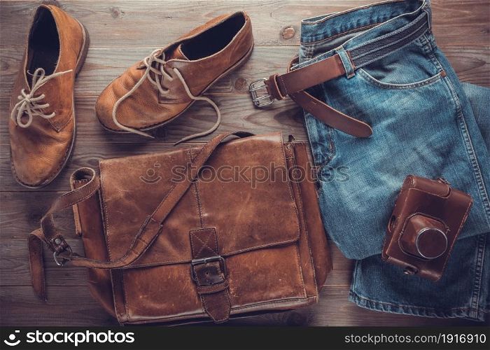 Denim jeans and old boots with leather bag at wood table. Travel concept of retro clothes
