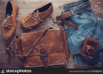 Denim jeans and old boots with leather bag at wood table. Travel concept of retro clothes