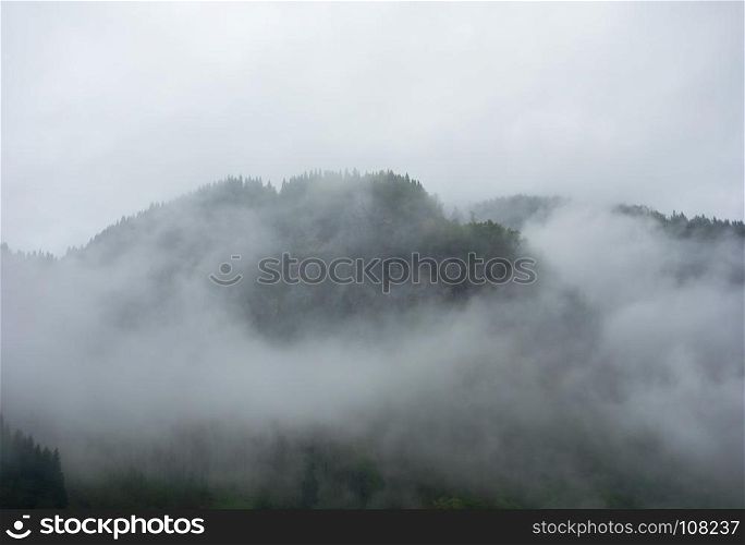 Dense fog and clouds covering forested mountain in Norway.