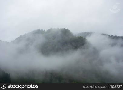 Dense fog and clouds covering forested mountain in Norway.