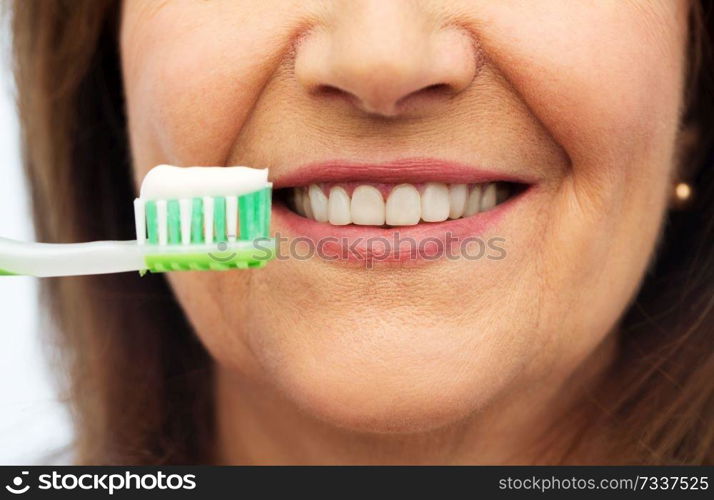 dental care and hygiene people concept - close up of smiling senior woman with toothbrush brushing her teeth over white background. senior woman with toothbrush brushing her teeth