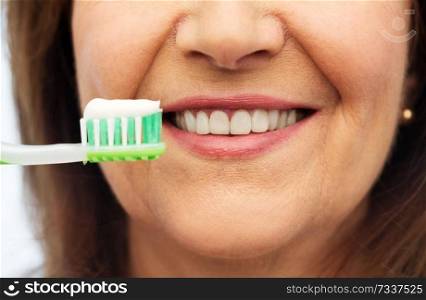 dental care and hygiene people concept - close up of smiling senior woman with toothbrush brushing her teeth over white background. senior woman with toothbrush brushing her teeth
