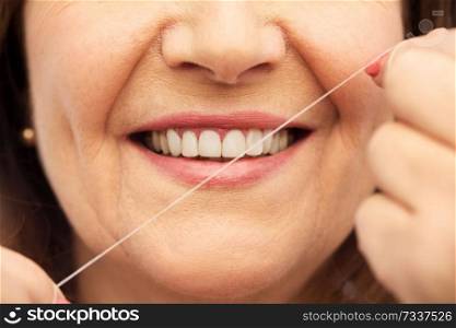 dental care and hygiene people concept - close up of smiling senior woman cleaning her teeth by floss over white background. senior woman cleaning her teeth by dental floss