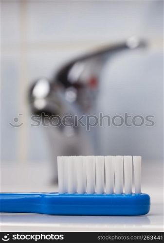 Dental care health concept. Closeup blue brush toothbrush in bathroom on sink, faucet in the background