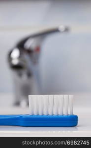 Dental care health concept. Closeup blue brush toothbrush in bathroom on sink, faucet in the background