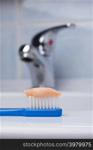 Dental care health concept. Closeup blue brush toothbrush with paste in bathroom on sink, faucet in the background