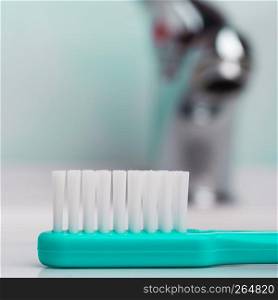Dental care health concept. Closeup green brush toothbrush in bathroom on sink, faucet in the background