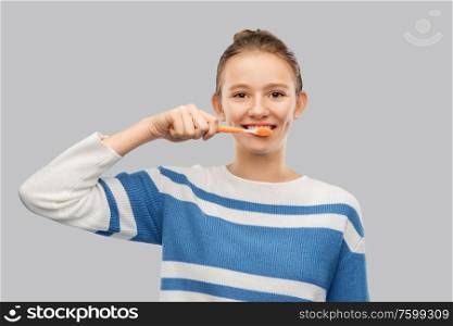 dental care, hygiene and people concept - happy smiling teenage girl in pullover brushing teeth with toothbrush over grey background. happy teenage girl brushing teeth with toothbrush