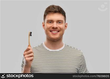 dental care, oral hygiene and people concept - happy smiling young man with wooden toothbrush over gray background. smiling man with wooden toothbrush