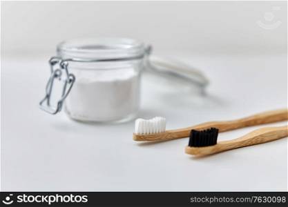 dental care, sustainability and eco living concept - washing soda in glass jar and wooden toothbrushes on white background. washing soda and wooden toothbrushes