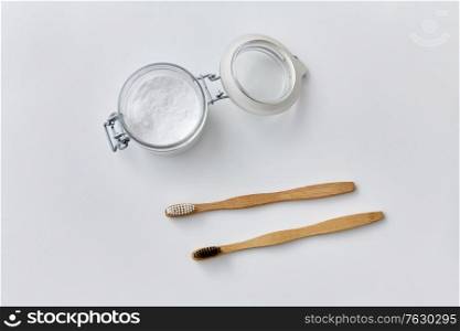 dental care, sustainability and eco living concept - washing soda in glass jar and wooden toothbrushes on white background. washing soda and wooden toothbrushes