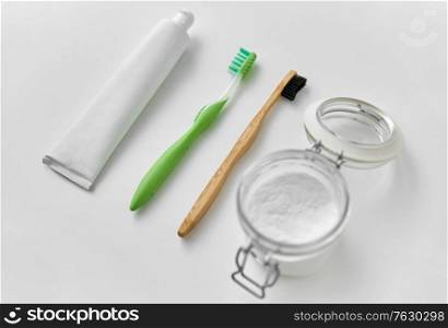 dental care, sustainability and eco living concept - wooden and plastic toothbrush, toothpaste and washing soda in glass jar on white background. toothbrushes, toothpaste and soda in jar