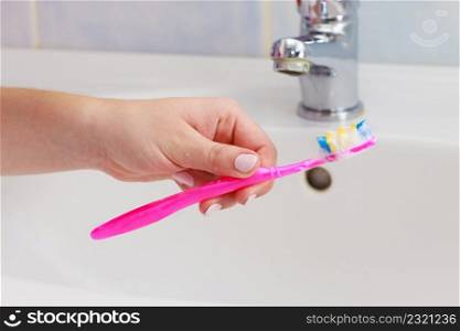Dental care. Woman hands is holding toothbrush with toothpaste in bathroom, sink and faucet in background. Hand holding toothbrush in bathroom