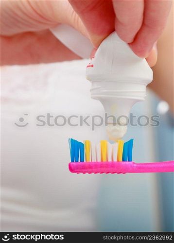 Dental health care. Closeup woman hands is holding toothbrush and placing toothpaste on it.